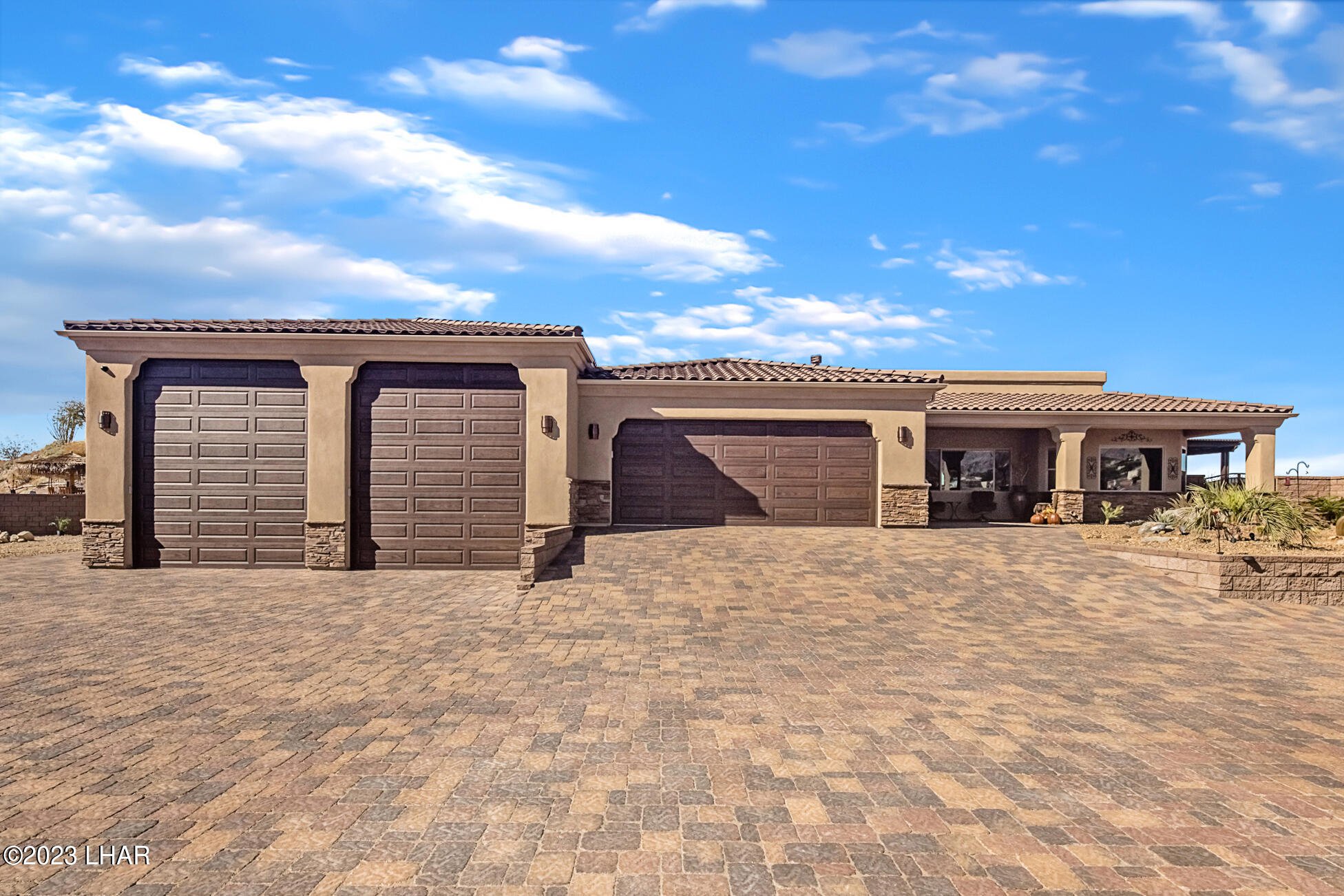 Lake Havasu home with two tall motorhome garage doors, a conventional garage and a wide paved approach